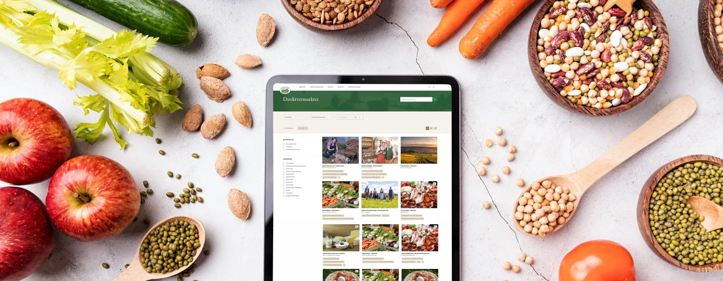 Abbildung der neuen "Gutes vom Bauernhof"-Website auf einem Tablet. Umgeben von verschiedenem Obst und Gemüse auf einem weißen Tisch