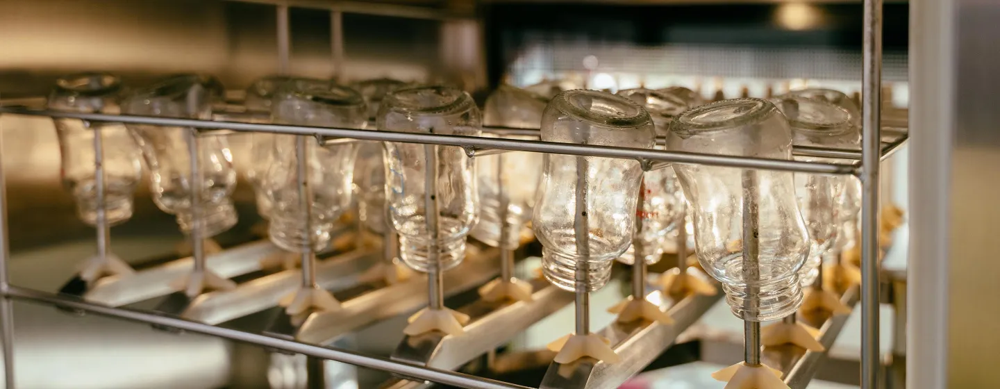 Mehrere durchsichtige Kunststoffflaschen hängen kopfüber an einer Metallstange zum Trocknen oder Sterilisieren.