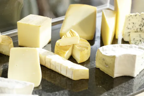 Verschiedene Käsesorten in unterschiedlichen Formen, darunter runde, rechteckige und keilförmige Stücke, auf einer dunklen Oberfläche.