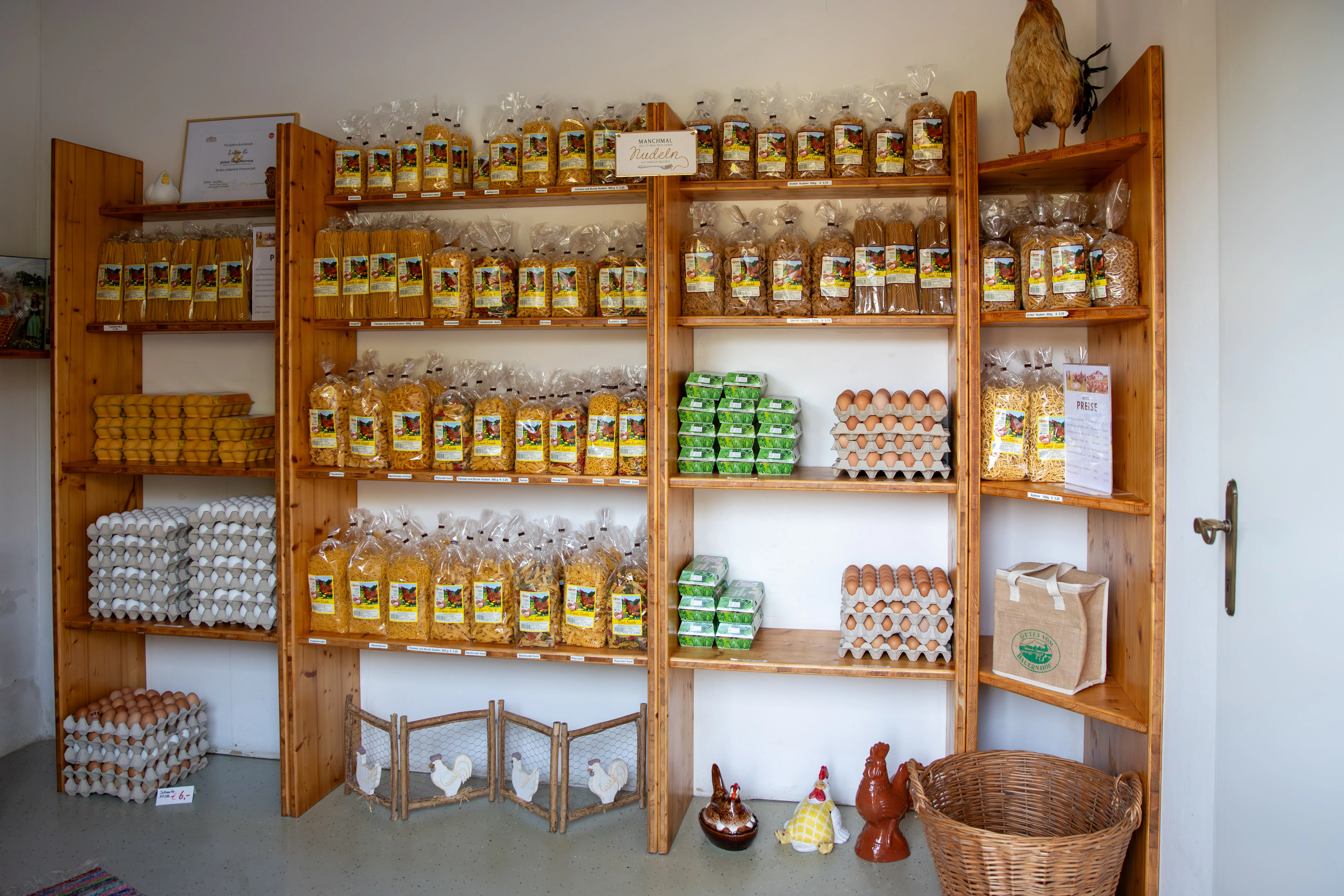 Braune Regale mit verschiedenen Packungen Nudeln, Eiern und Dekomaterial, weiße Wand
