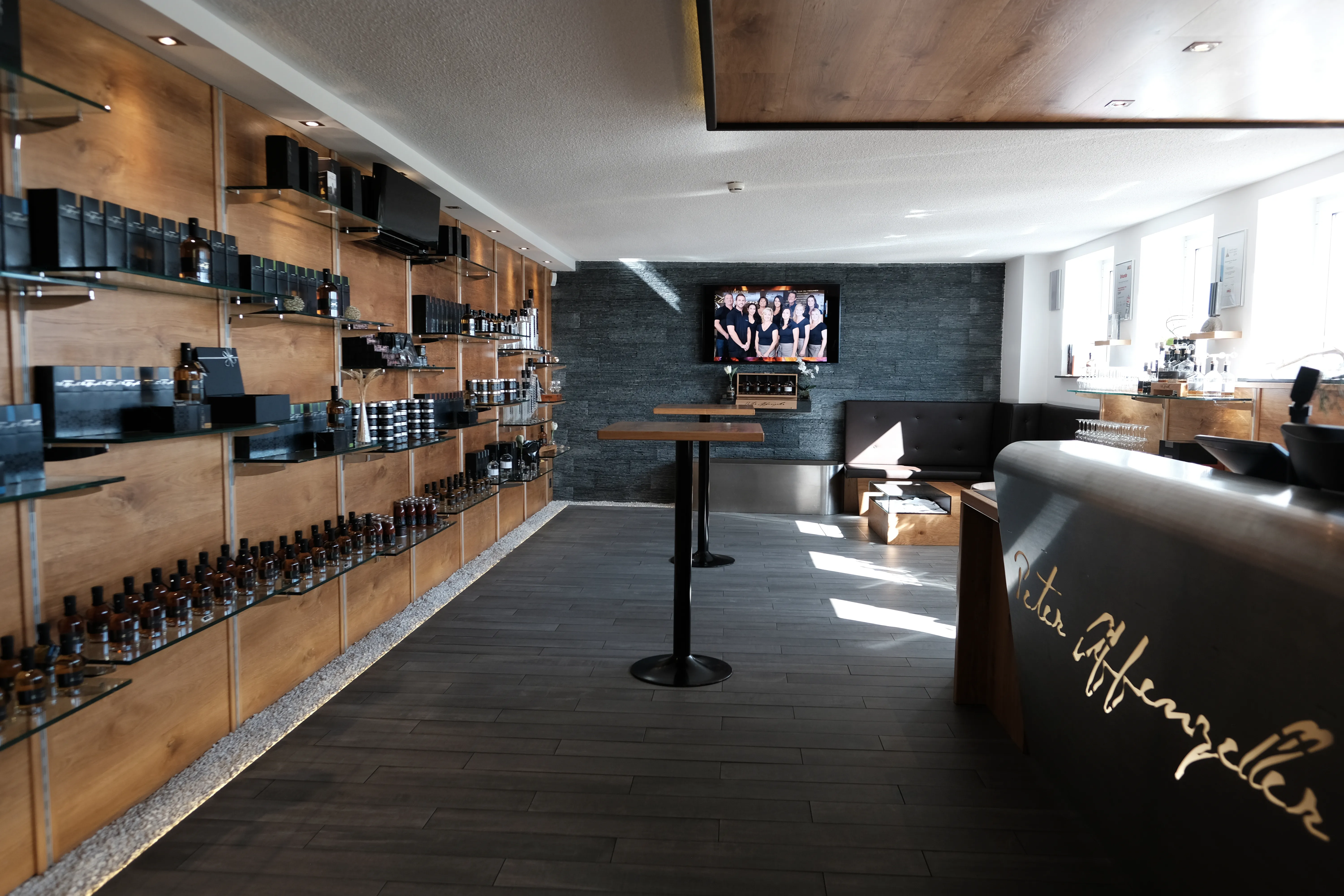 braune Regale mit dunklen Produkten an der Wand, schwarzer Boden, Stehtische und weiße Decke