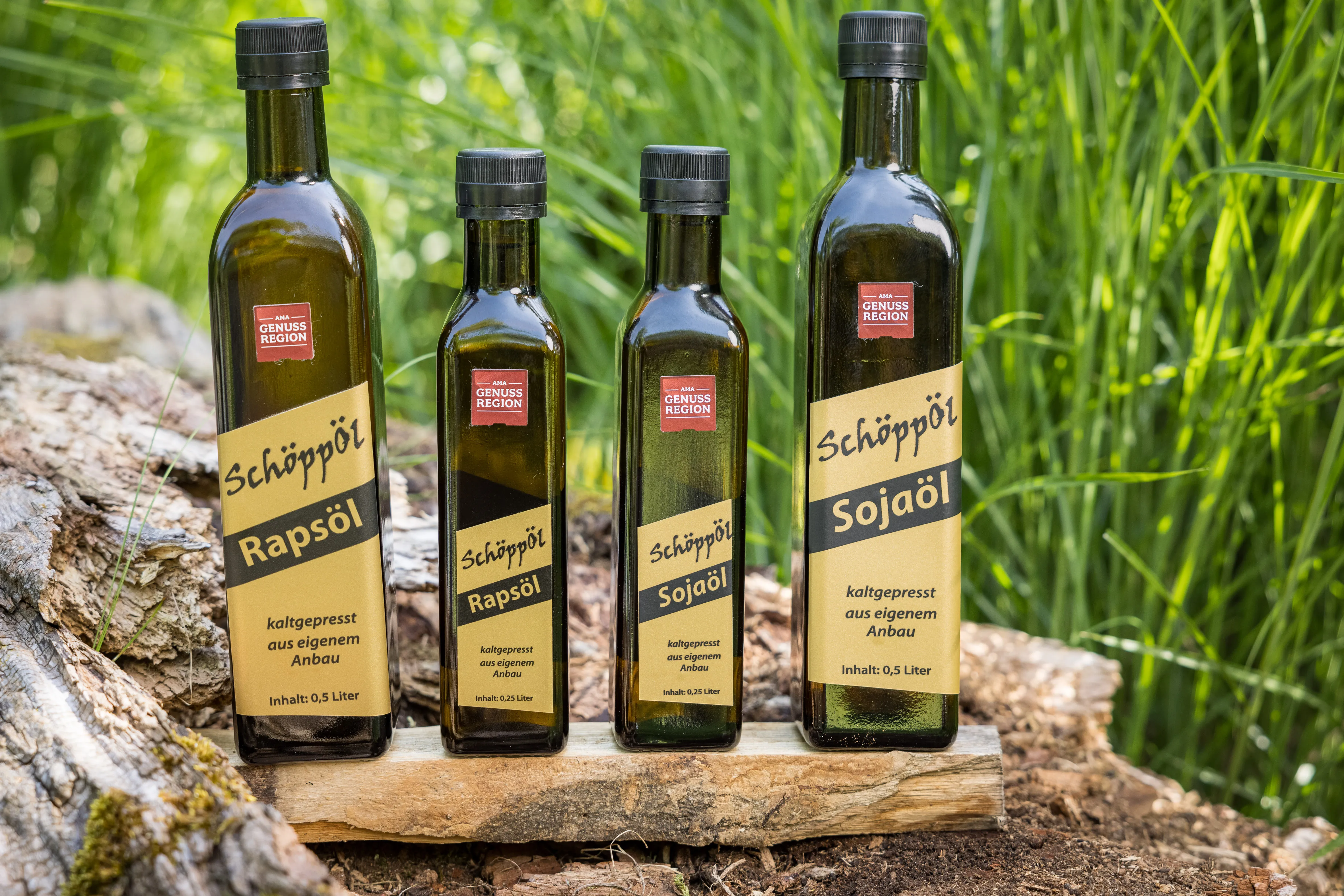 Auf einem Holzbrett stehen vier dunkelgrüne Flaschen mit gelben Etikett . Dahinter grünes Gras.
