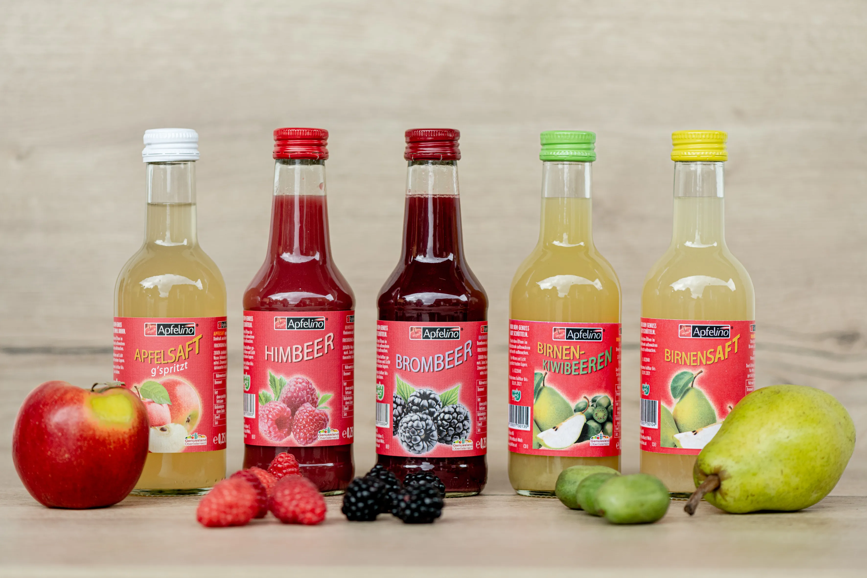 verschieden färbige Flaschen stehen auf hellbeigen Boden bzw. Hintergrund beige, daneben ein Apfel eine Birne und weitere Früchte