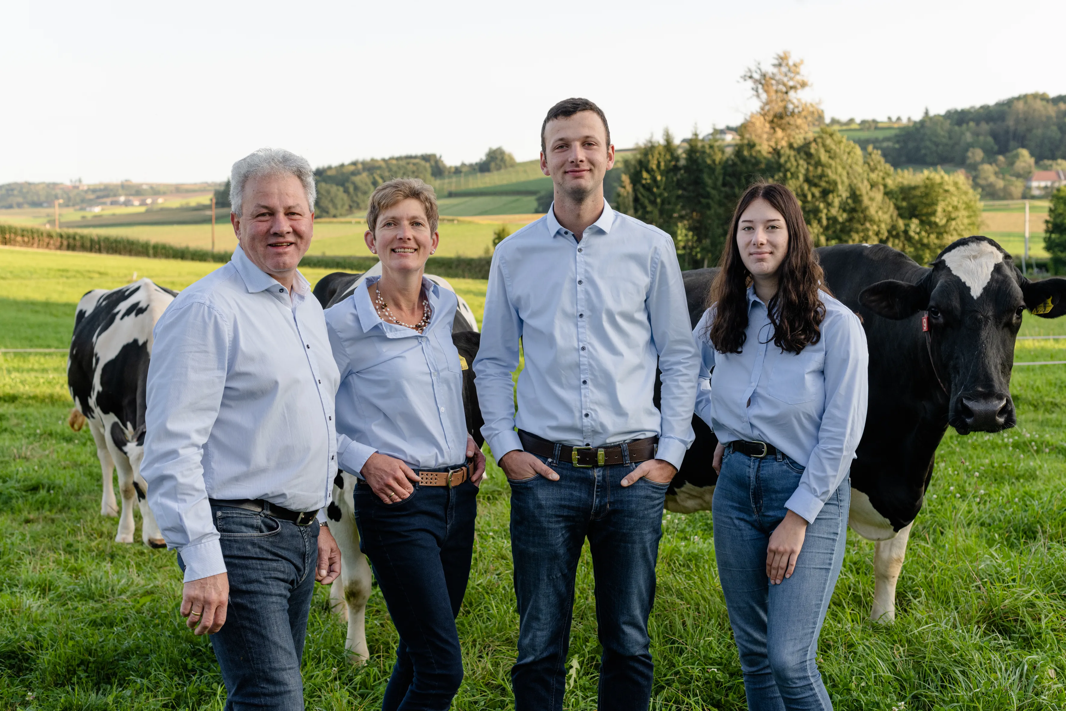 Zwei Männer und zwei Frauen stehen auf einer Wiese, im Hintergrund Kühle