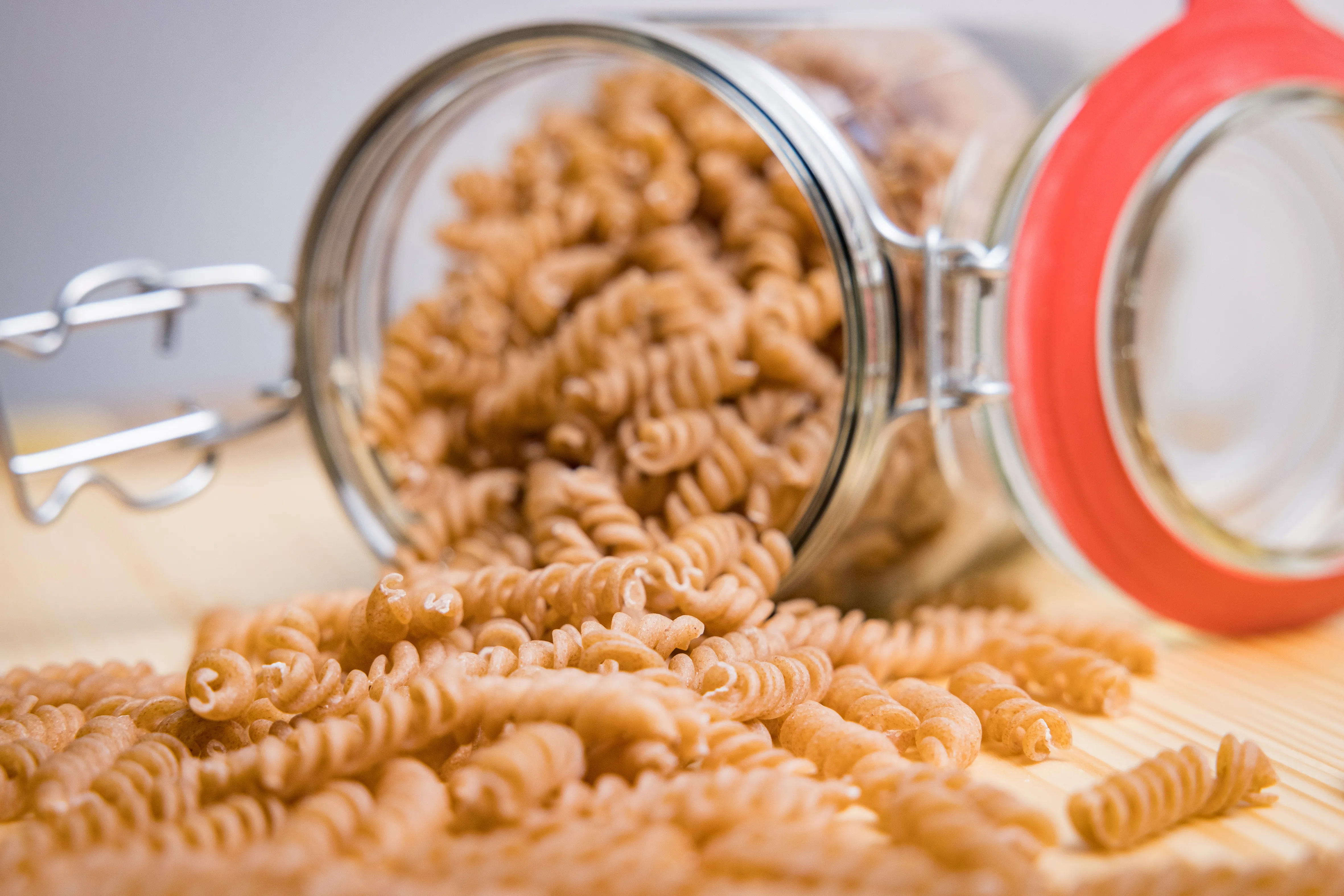 Auf einem hellen Tisch liegt ein Glas geöffnet, daraus fallen Spiralnudeln
