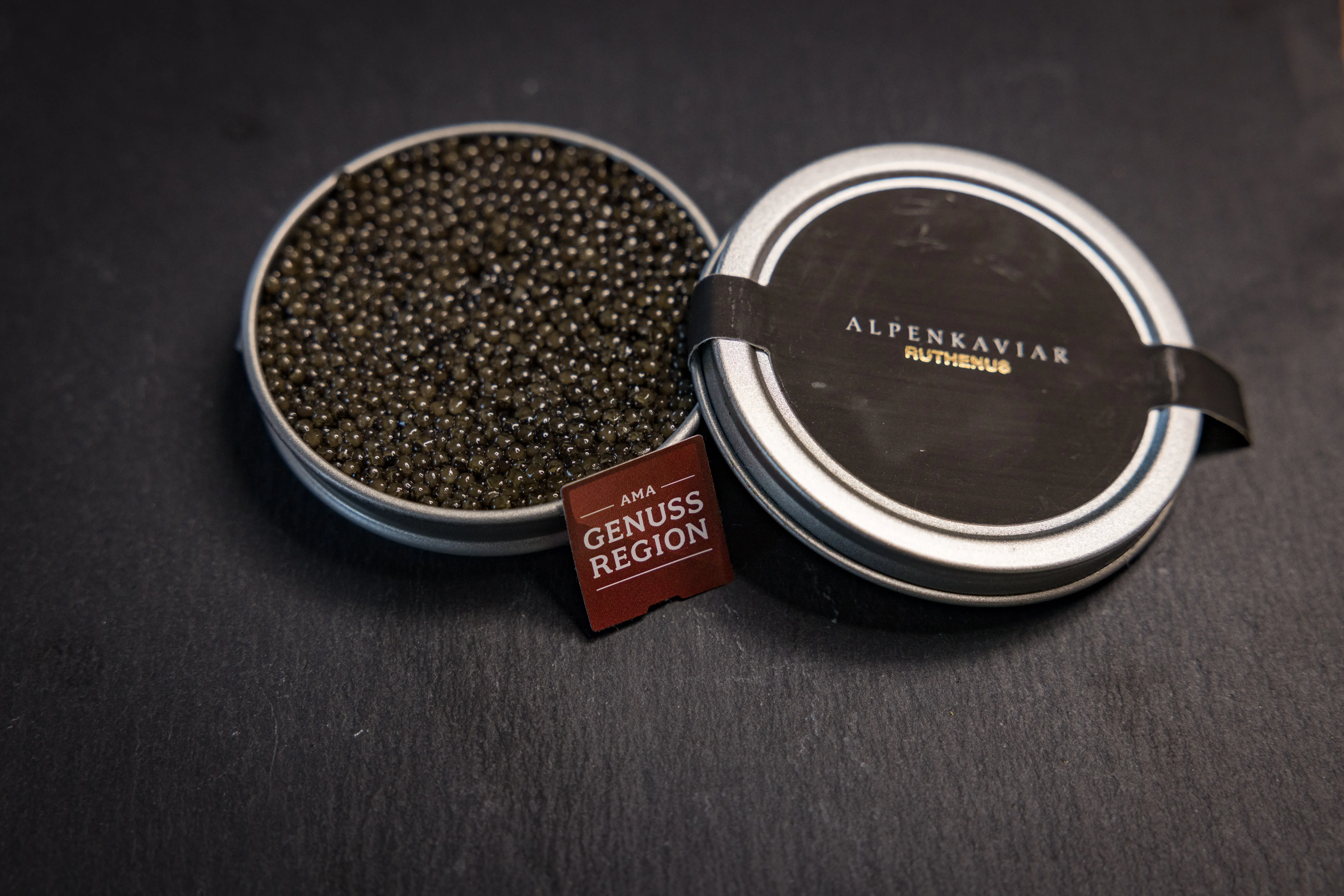 Auf schwarzem Untergrund steht eine silberfarbene Dose mit schwarzem Kaviar.