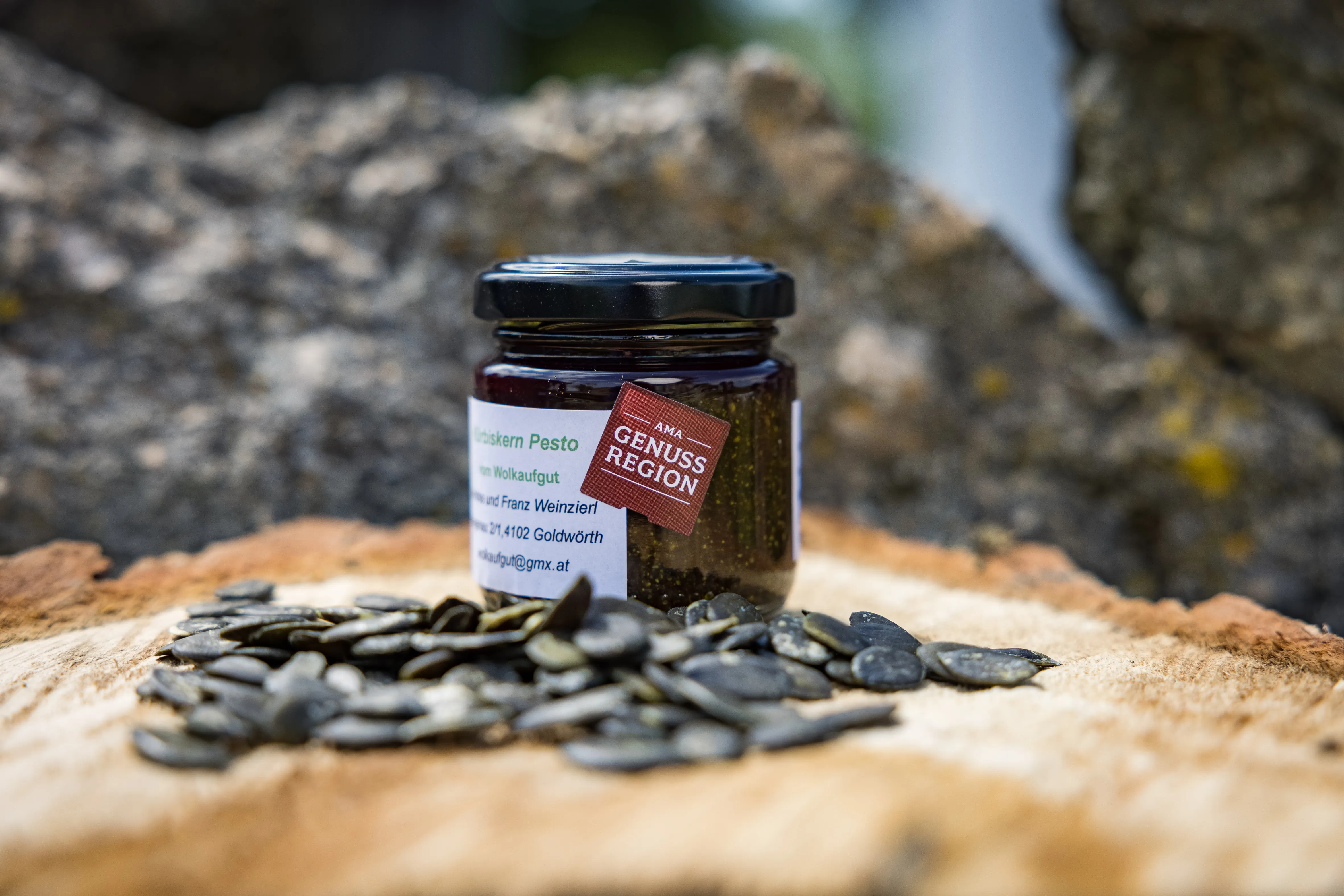 Auf einem Holzstumpf steht ein Glas mit Pesto, daneben liegen Kürbiskerne, dahinter ein Stein.