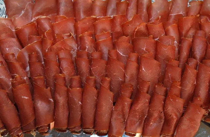 Von oben gesehen sieht man mageren Speck aufgeschnitten und zu Rollen geformt geschlichtet