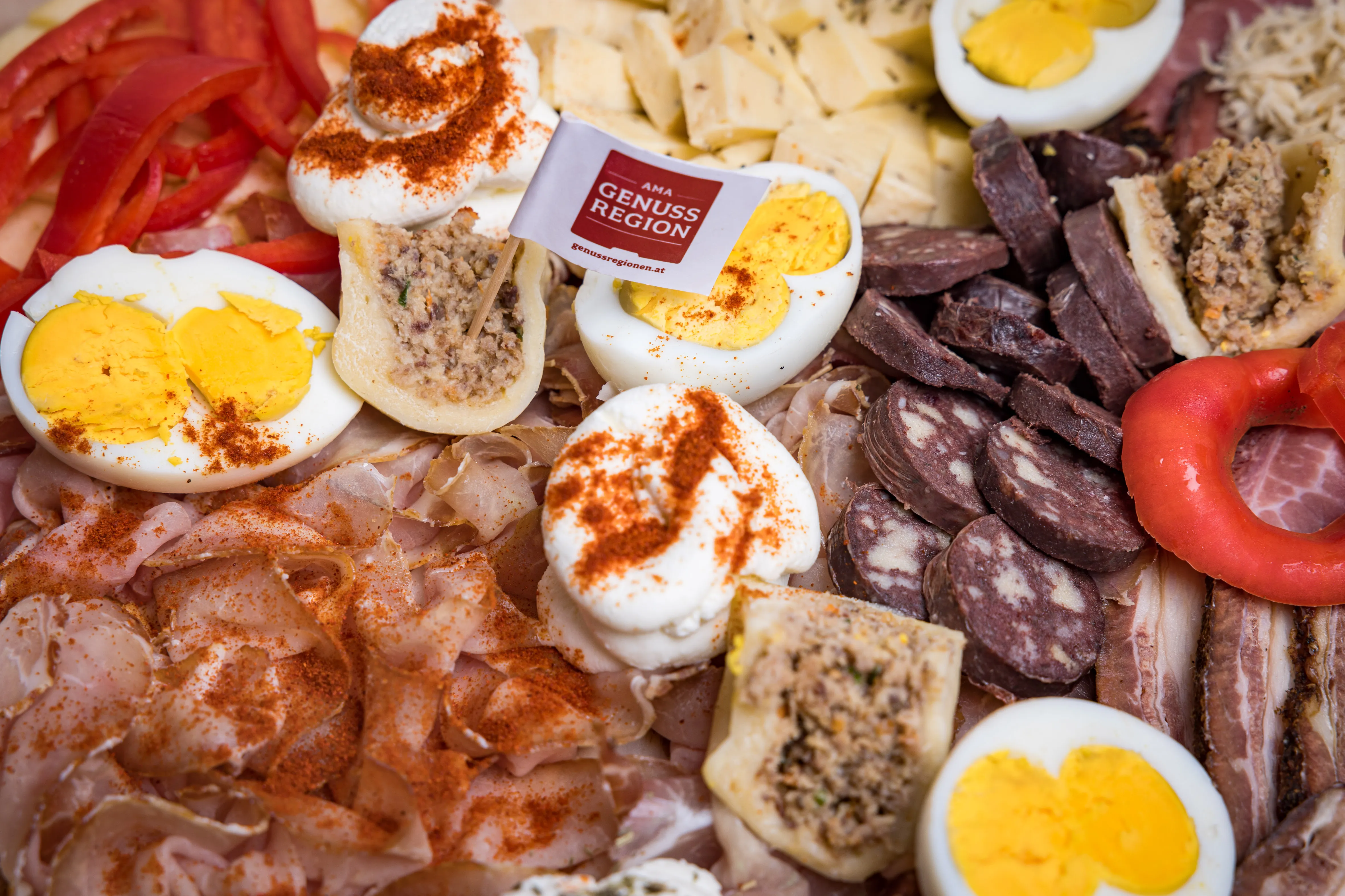 Auf dem Bild sieht man verschiedene Fleischprodukte aufgeschnitten, garniert mit Eier und Paprika