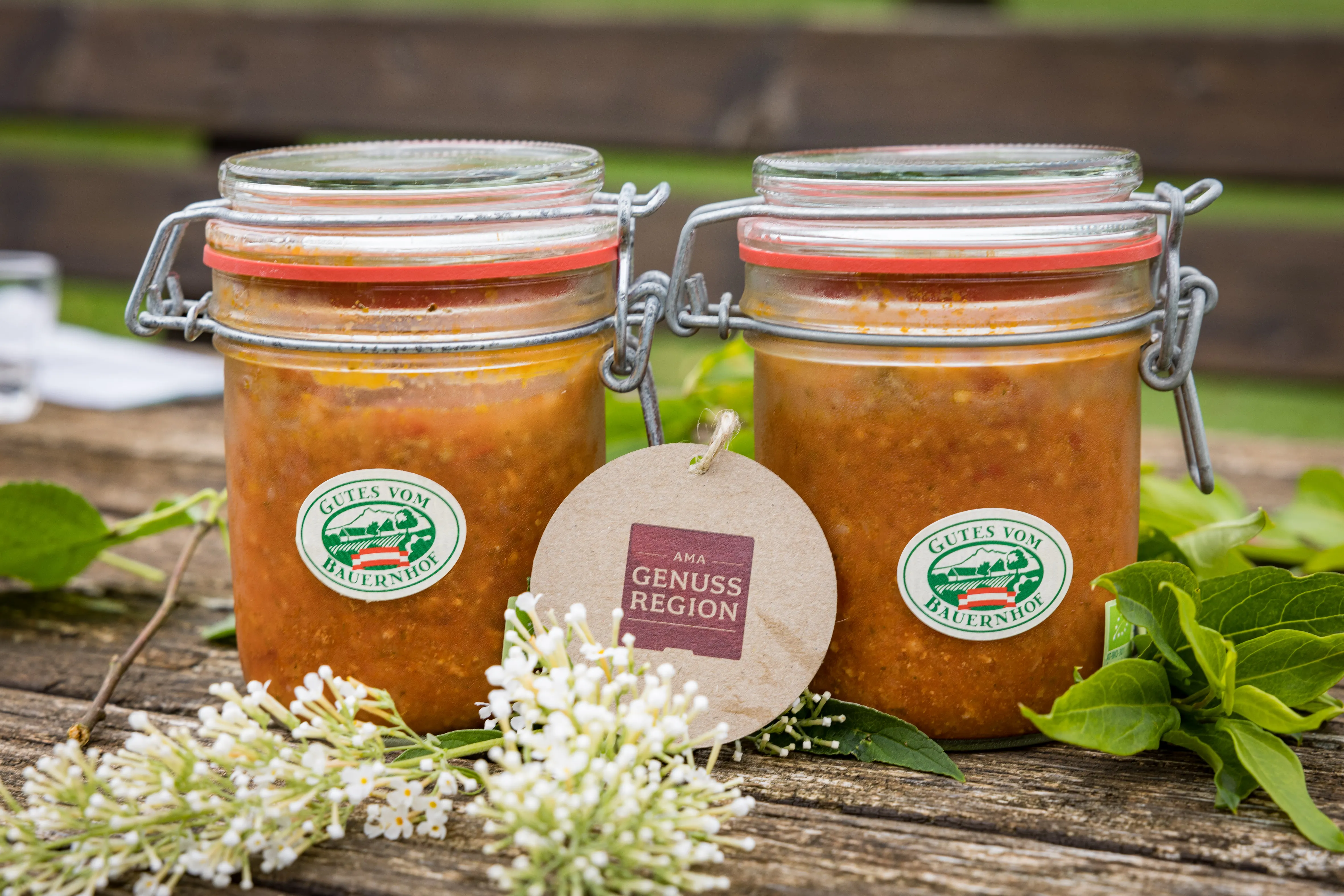 Auf einem Holztisch stehen zwei Einmachgläser mit orangefarbenen Inhalt, daneben Kräuter und Blüten zur Dekoration