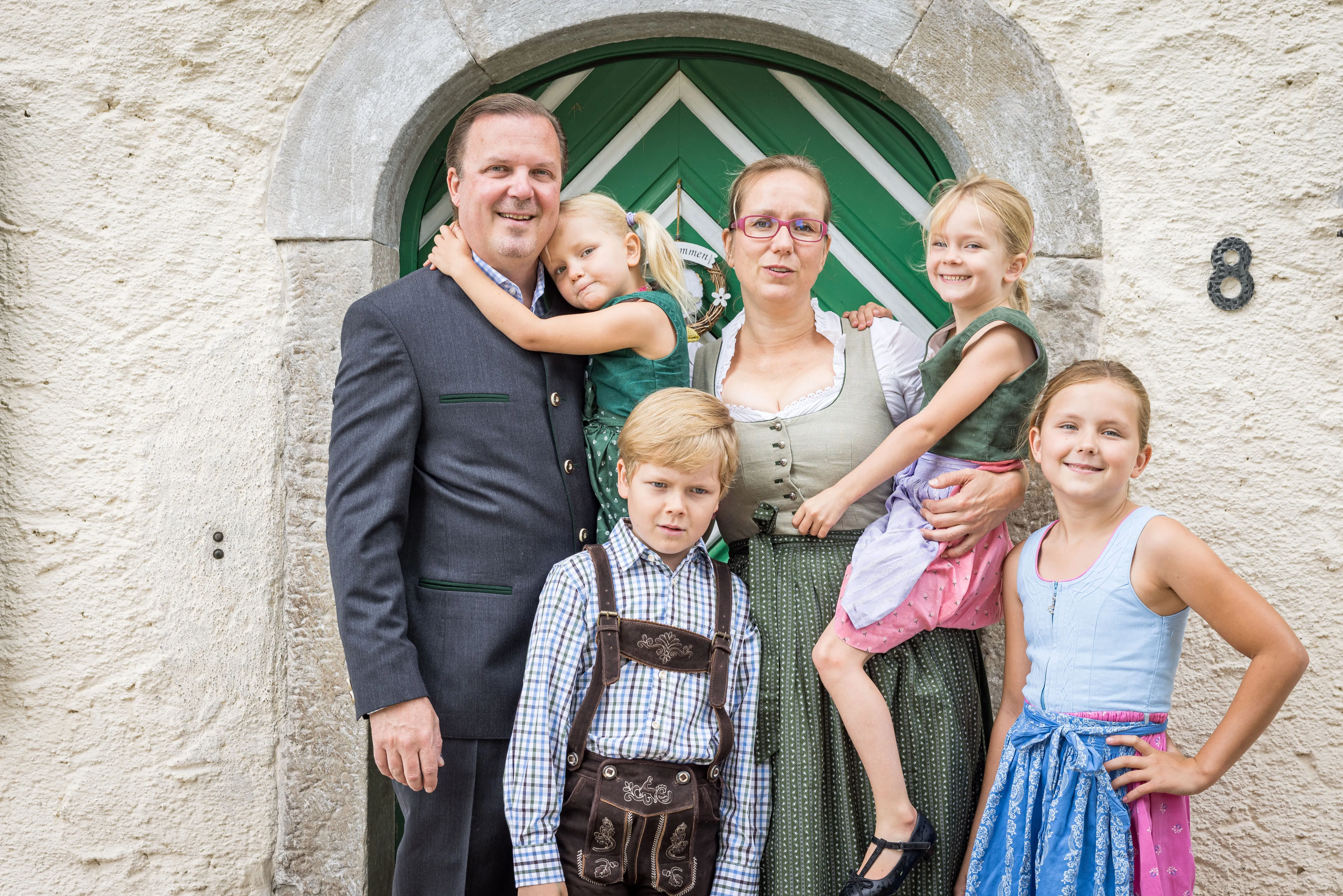 Vor einem grün/weißen Hoftor stehen eine Frau, ein Mann und ihre vier Kinder, alle in Dirndl Trachtenanzug bzw. Lederhose