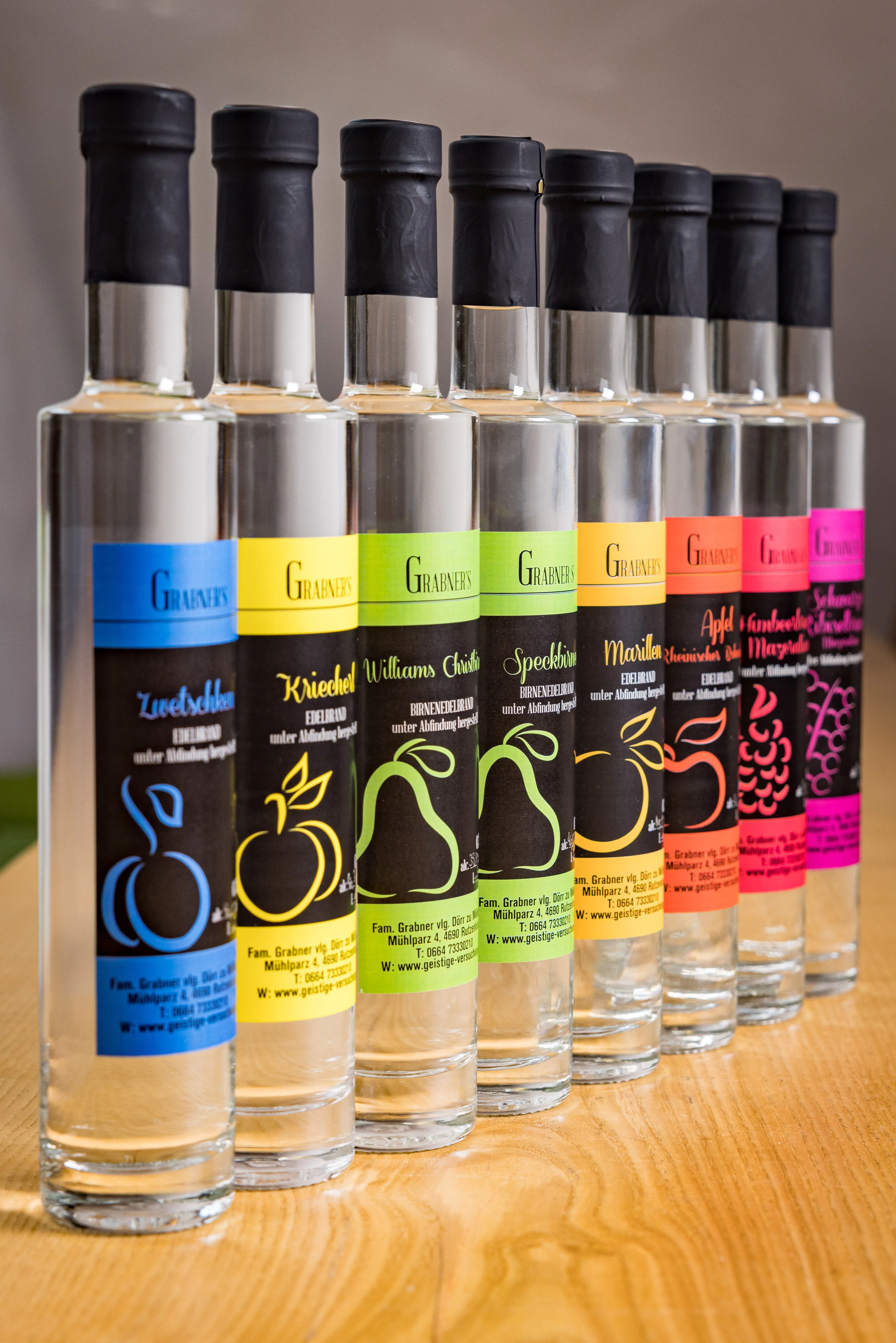 Mehrere Flaschen mit verschieden farbigen Etiketten stehen in Reih und Glied auf einem Holztisch