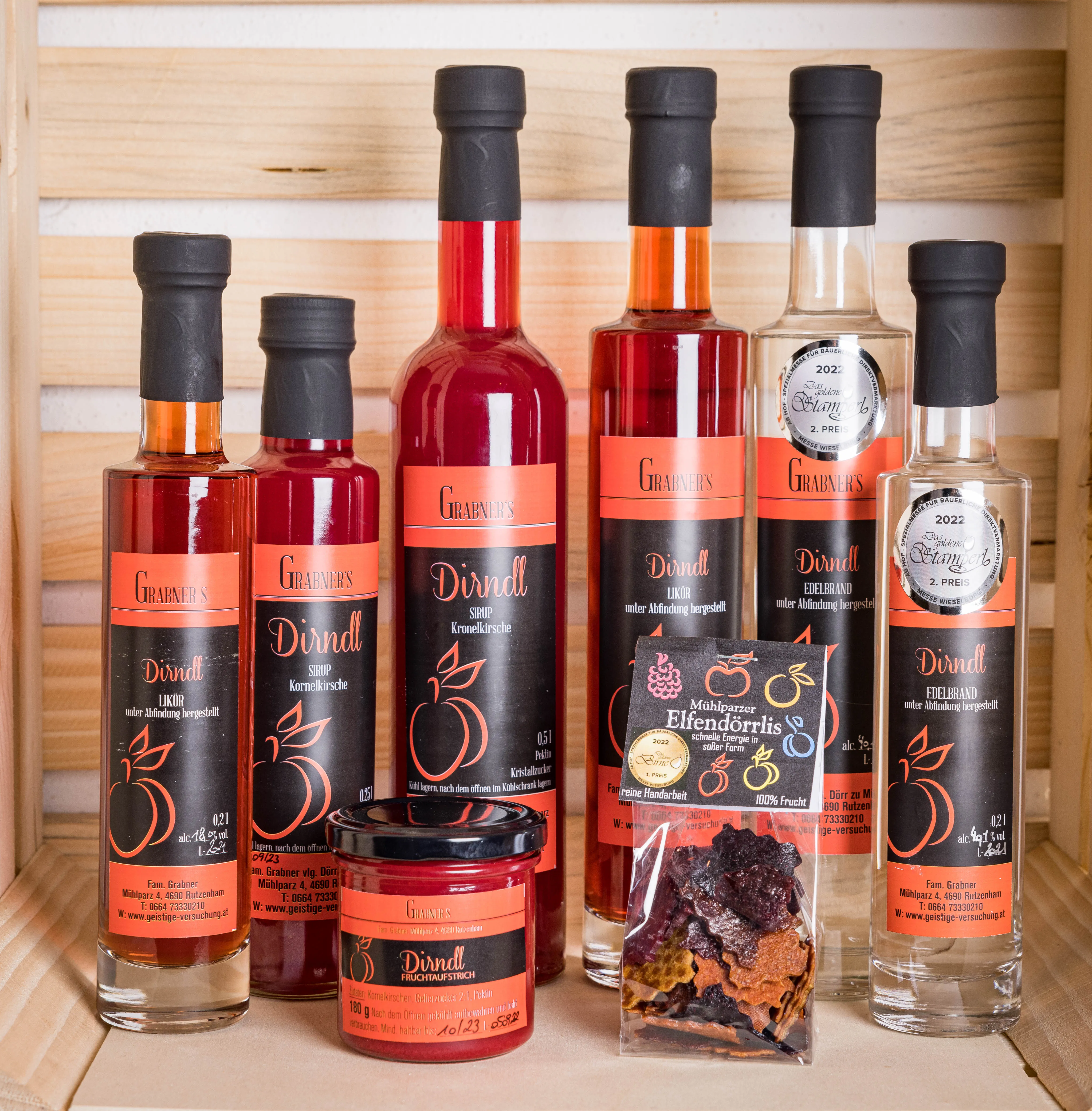 Auf einem hellen Regal stehen verschieden große Flaschen mit rotem bzw. hellem Inhalt. Davor auch ein Glas und Trockenfrüchte im Sackerl.