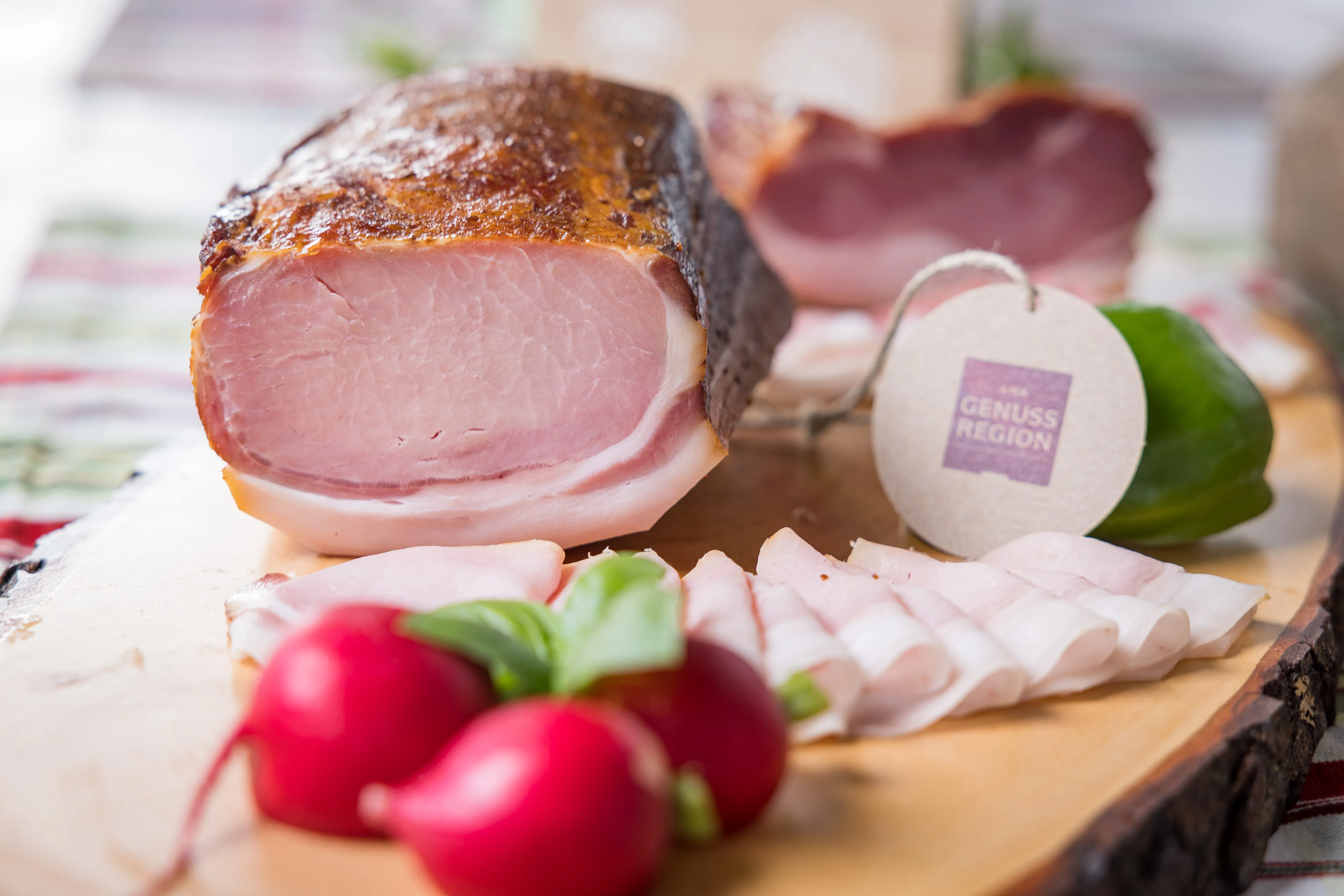 Auf einem Holzbrett liegen verschiedenen Speck- bzw. Wurstsorten, garniert mit roten Radischen