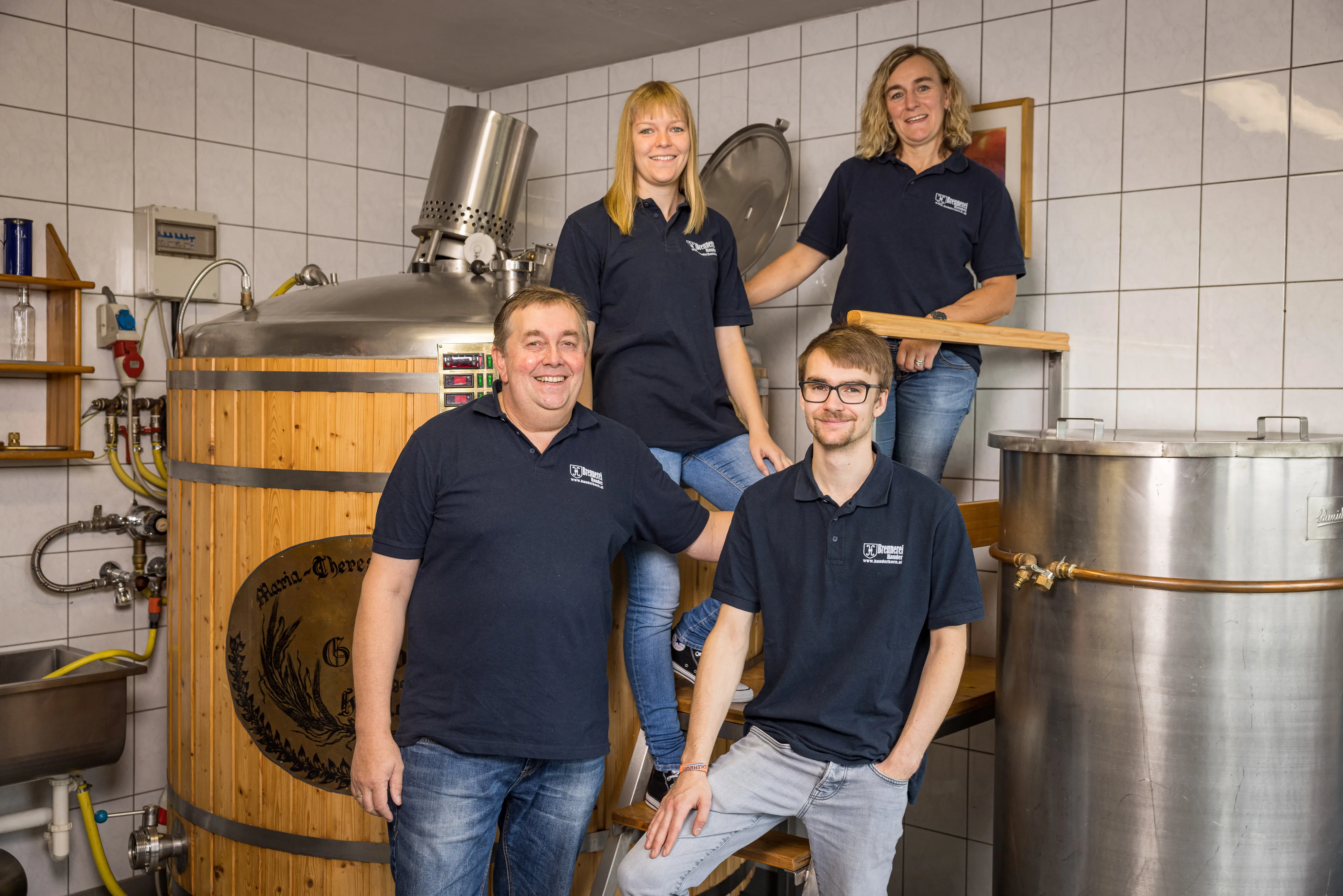 Zwei Frauen und zwei Männer mit dunkelblauen Polos und Jeans stehen neben bzw. vor einem großen Brennofen