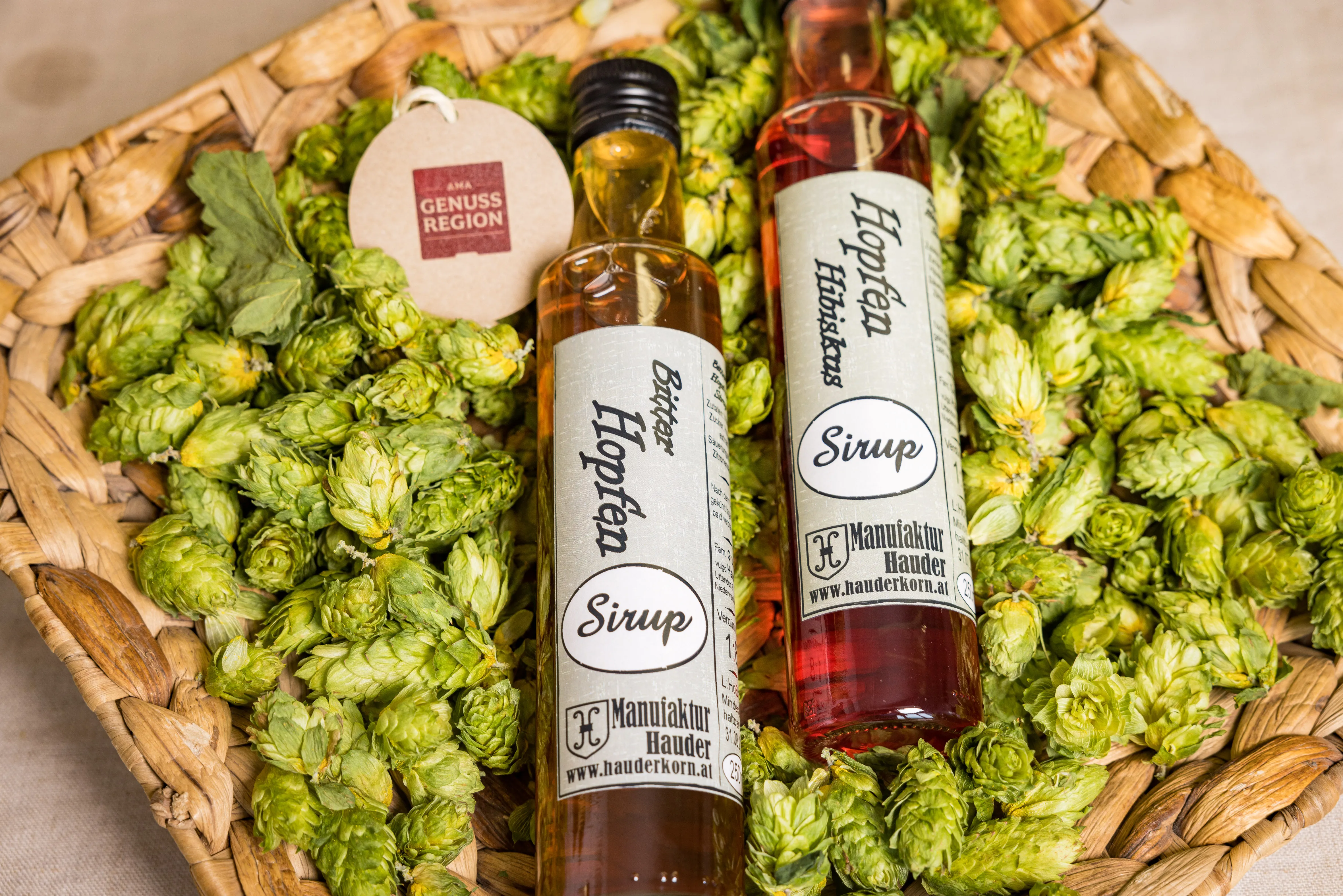 In einem Korb mit grünen Hopfenfrüchten liegen zwei Flaschen mit Hopfensirup