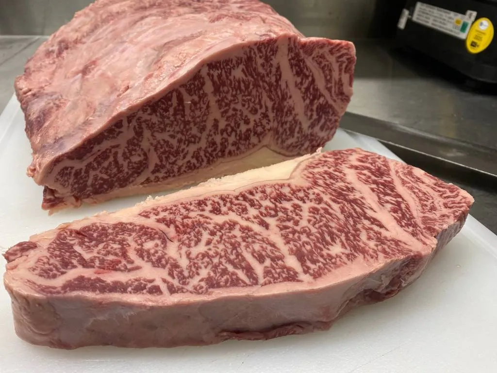 Auf dem Bild liegt auf einer weißen Unterlage ein Stück Frischfleisch und eine aufgeschnittene Scheibe Frischfleisch vom Rind
