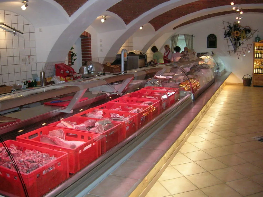 Man sieht einen großen Gewölberaum mit einer langen Fleischtheke, in welcher rote Kisten mit Fleischprodukten liegen; gelber gefliester Boden 