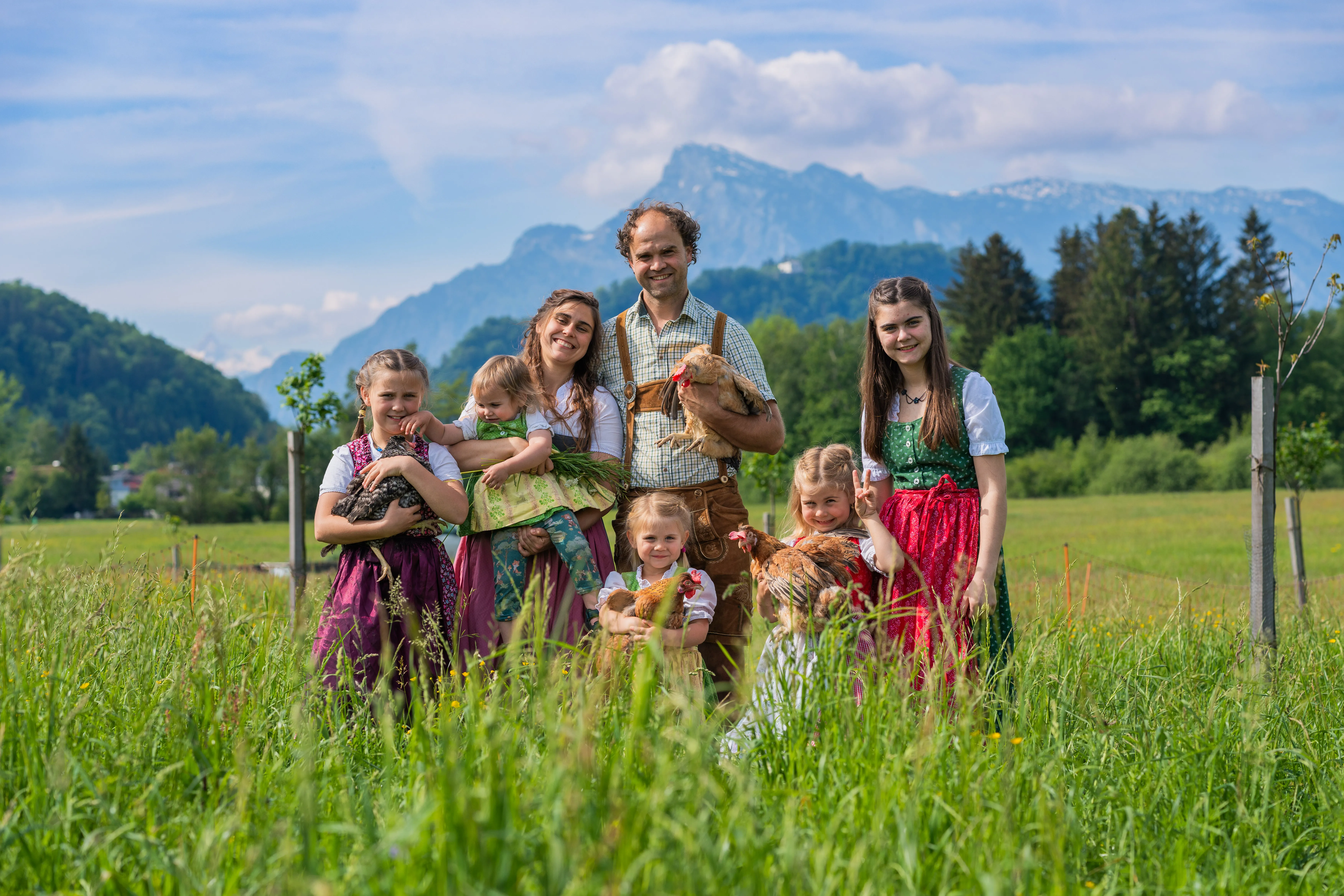 Familie Lettner mit 5 Kindern steht in der Tracht in der Wiese vor einem Bergpanorama