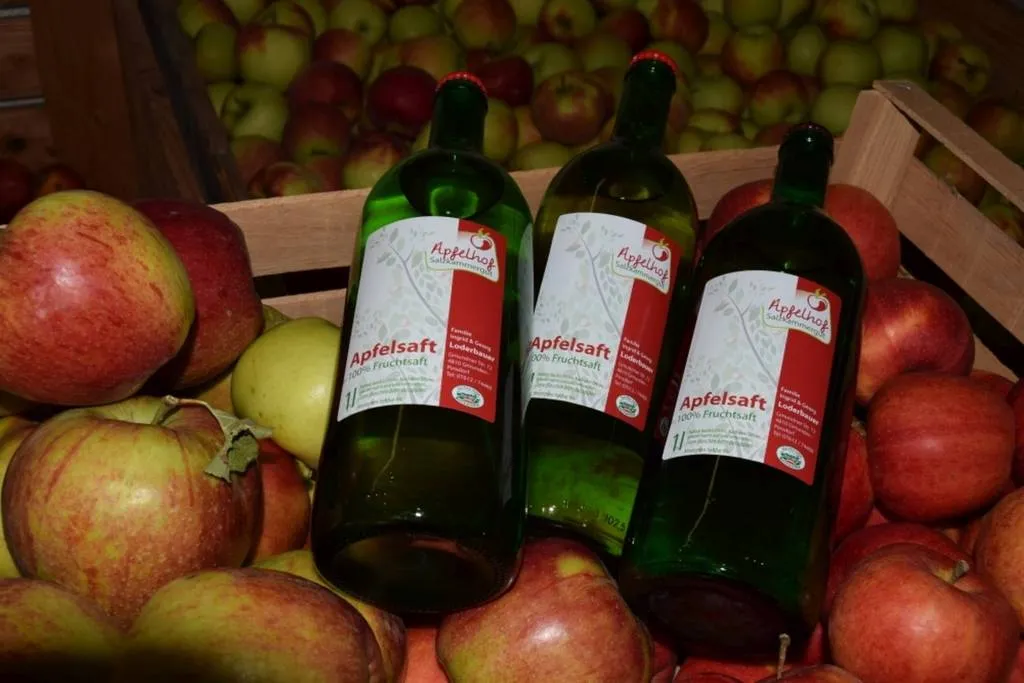 Auf dem Bild sieht man eine Kiste mit rot/gelben Äpfeln, darauf liegen drei Flaschen Apfelsaft.