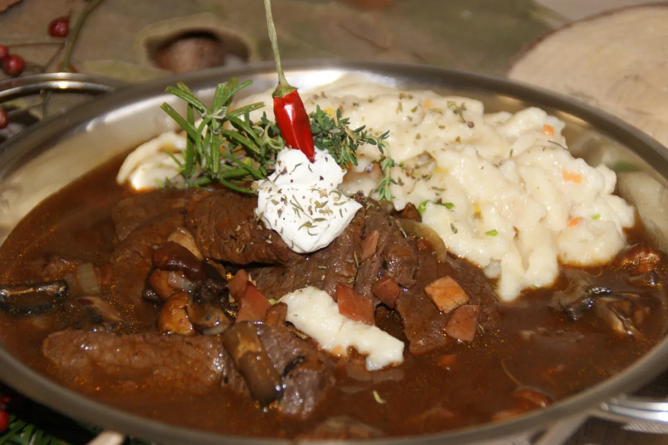 Wildragout mit dunkler Soße, garniert mit einem roten Chili, einem Klecks saurer Sahne und frischen Kräutern, dazu Spätzle mit Kräutern.