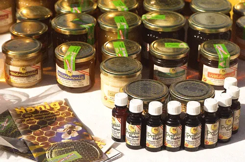 Auf einem weißen Untergrund stehen viele Gläser mit Honig, daneben mehrere Fläschchen mit Propolis, daneben einige Prospekte