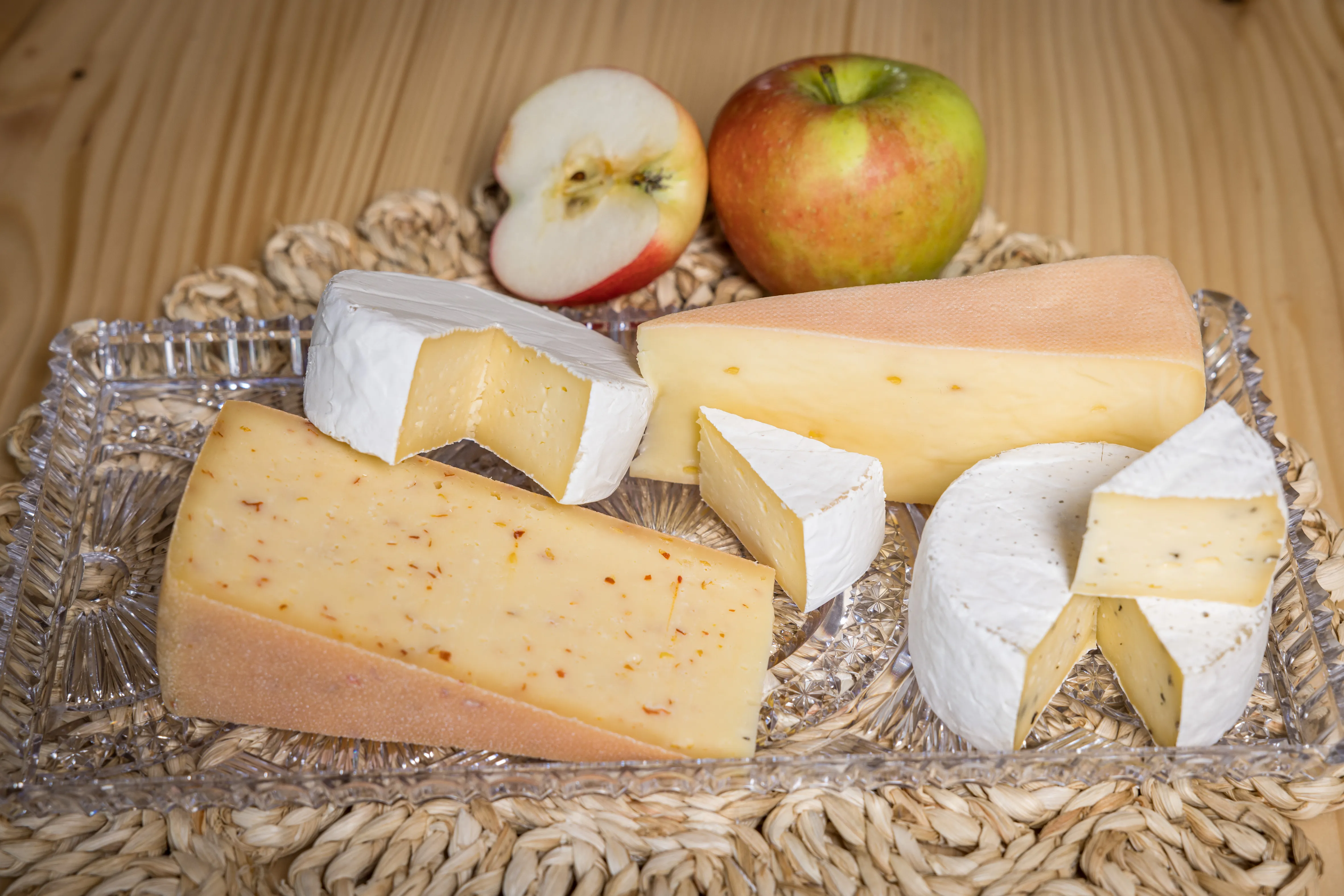 Auf einer Bastunterlage liegen mehrere Arten von Käse, daneben ein aufgeschnittener und ein ganzer Apfel