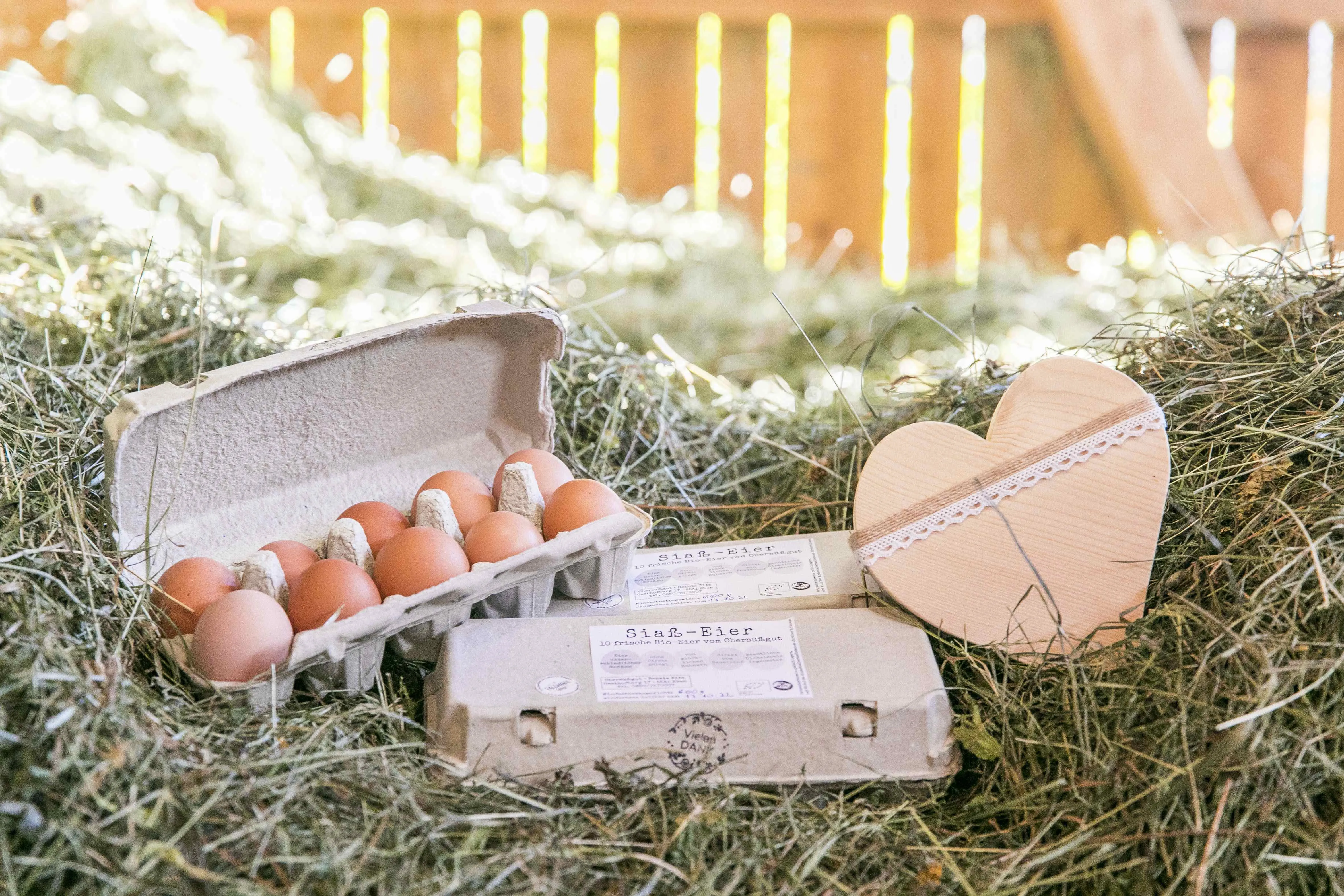 Eier liegen in einer Schachtel im Heu, am rechten Rand ein Holzherz