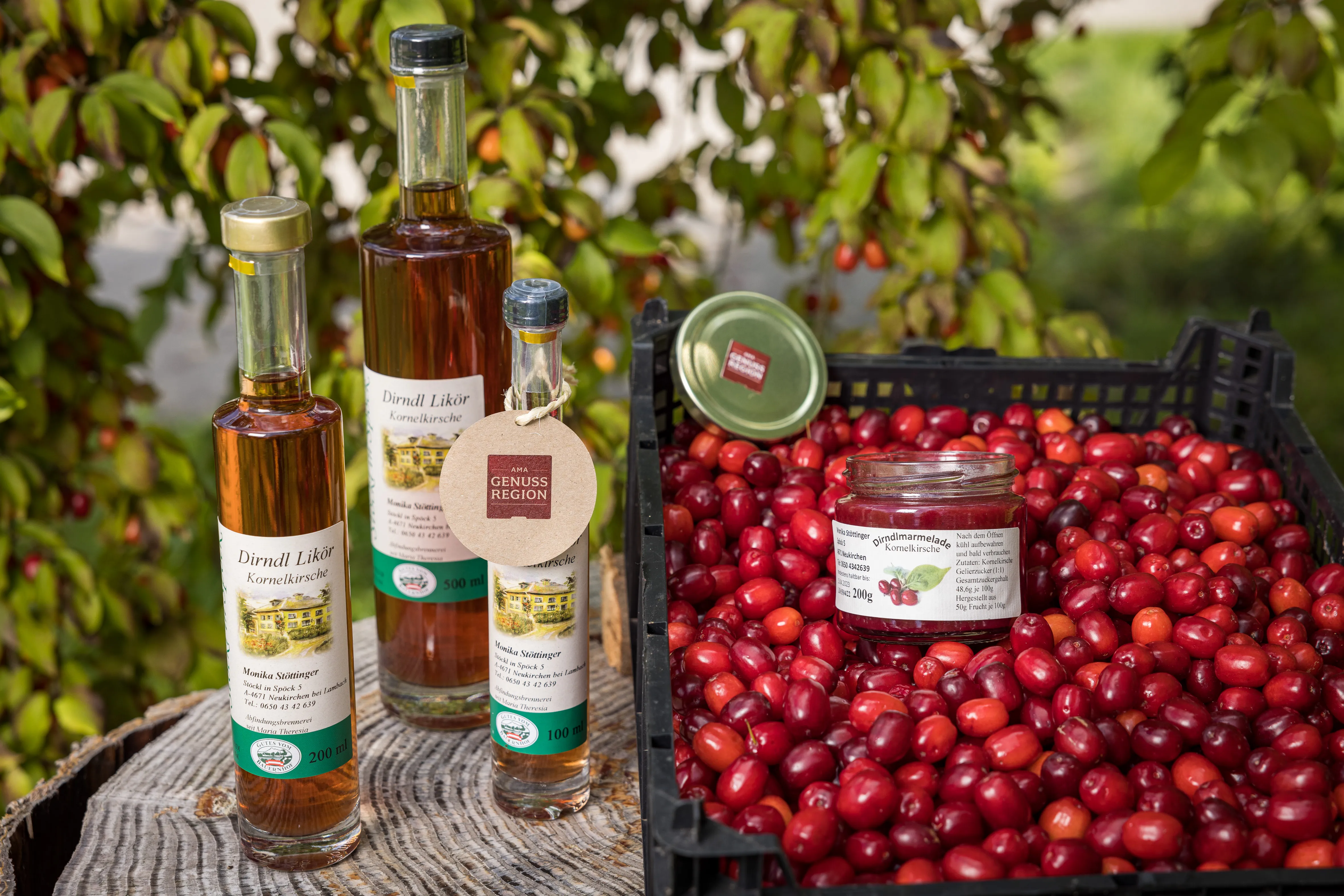 Auf einem Baumstumpf stehen drei Flaschen mit Dirndllikör, daneben eine Kiste mit frischen Dirndln und einem Glas Dirndlmarmelade