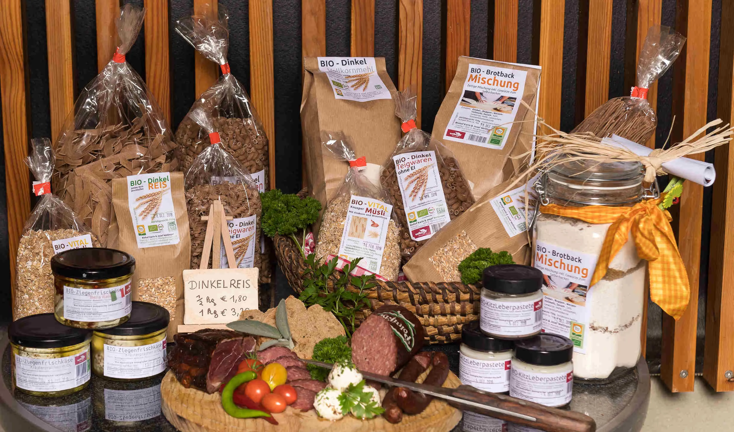 Verschiedene Gläser, Sackerl mit Getreide und aufgeschnittene Wurstspezialitäten liegen auf einem Brett bzw. tisch.