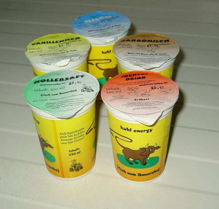Fünf farbenfrohe Becher mit Milchprodukten stehen auf weißem Untergrund