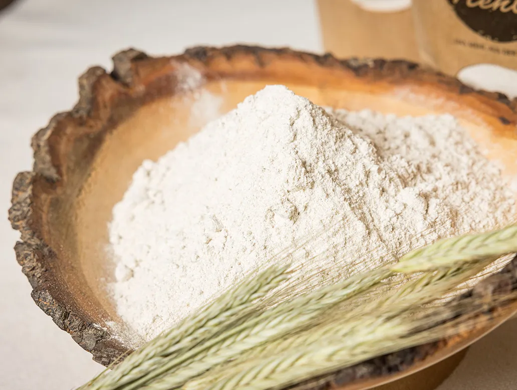 Holzschale mit einem Haufen weißem Mehl und zwei Ähren im Vordergrund.