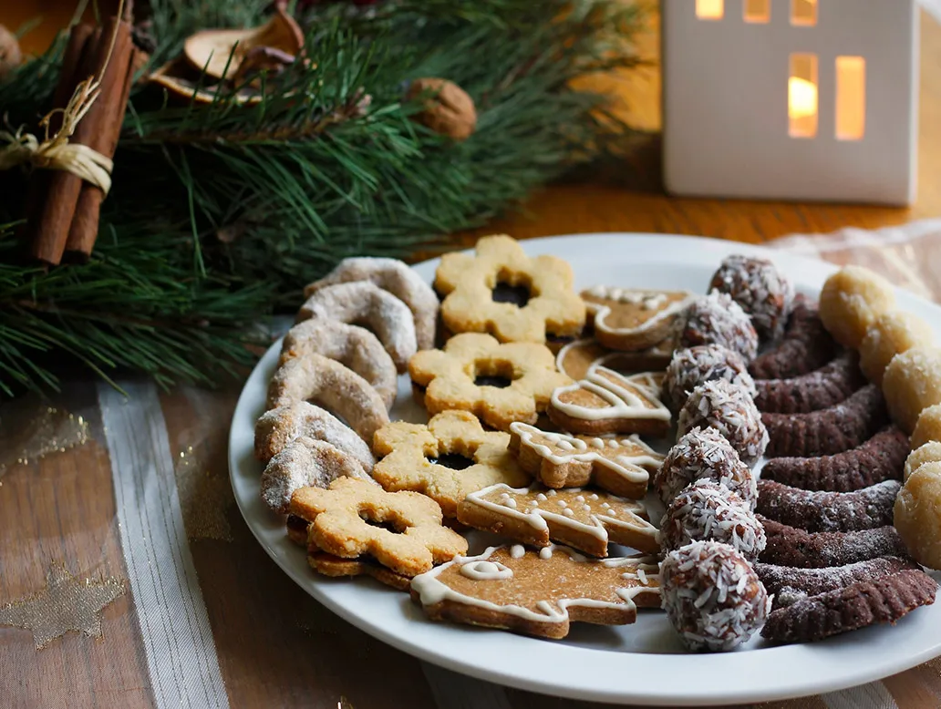 Teller mit verschiedenen Weihnachtsplätzchen, darunter blumenförmige, mit Puderzucker bestäubte, Lebkuchenfiguren mit Zuckerguss und Schokokugeln mit Kokosraspeln.