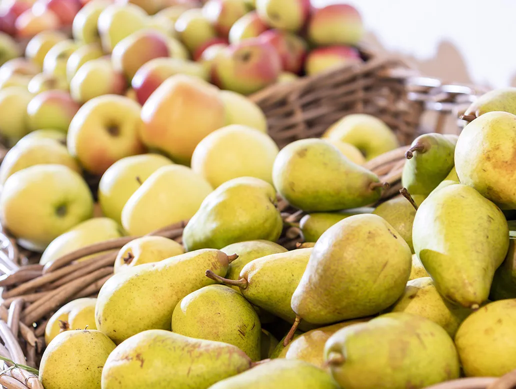 Nahaufnahme von mehreren grünen Birnen und Äpfeln in geflochtenen Körben.