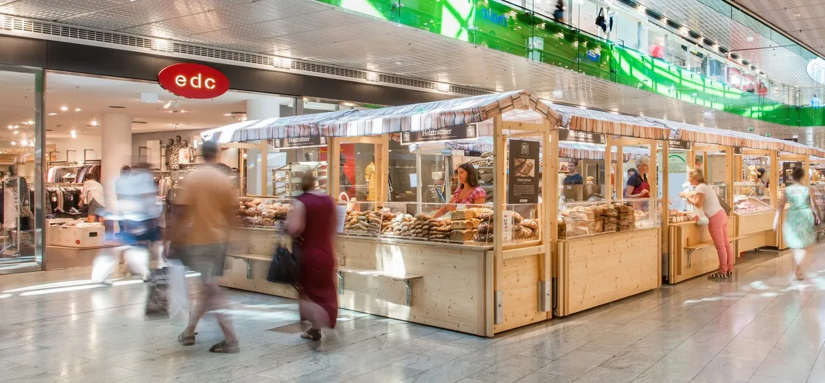 Bauernmarkt im Europark mit Holzständen und Person, die vorbei gehen