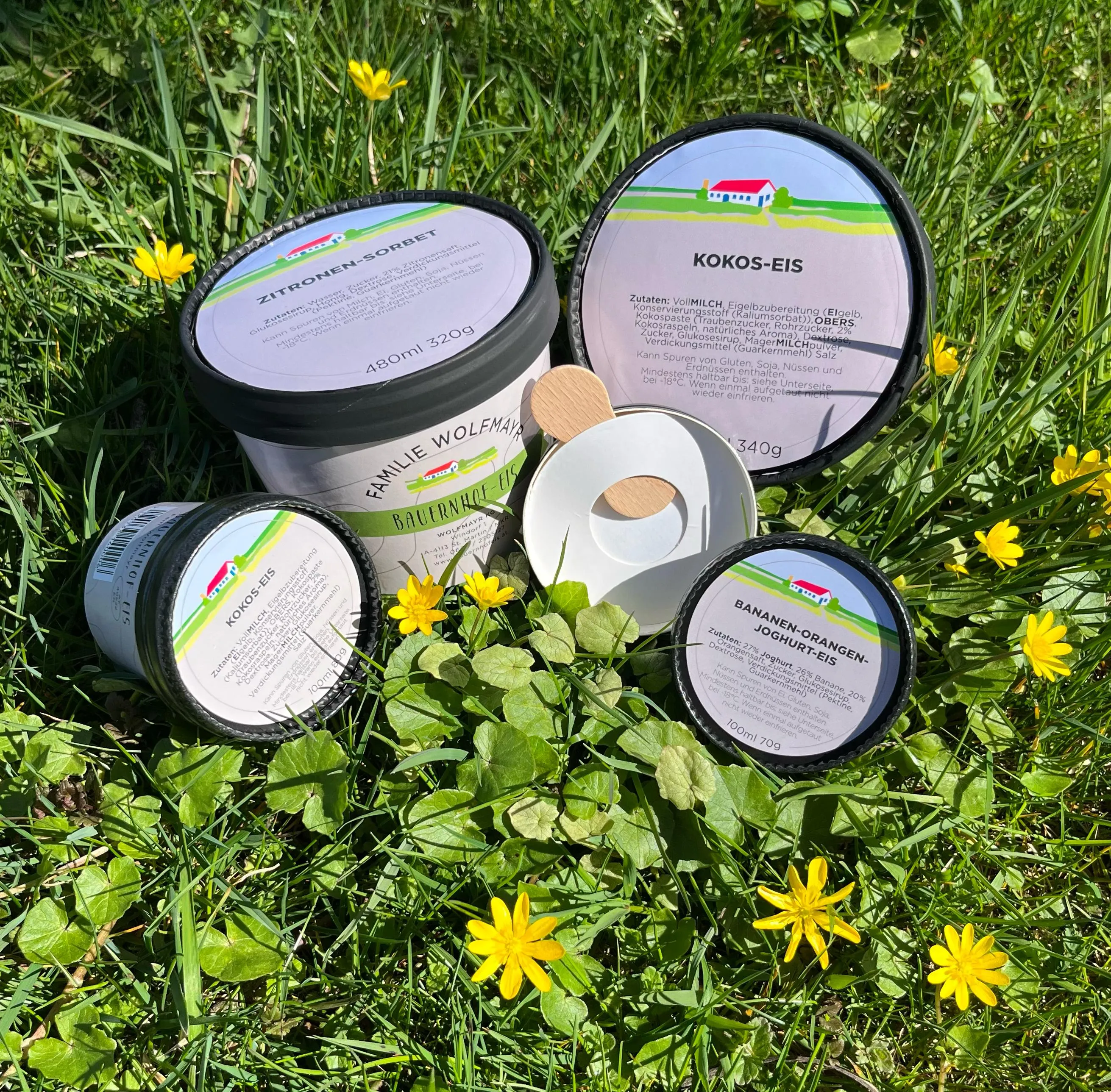 Auf einer grünen Wiese mit gelben Blumen liegen bzw. stehen mehrere Becher Speiseeis.