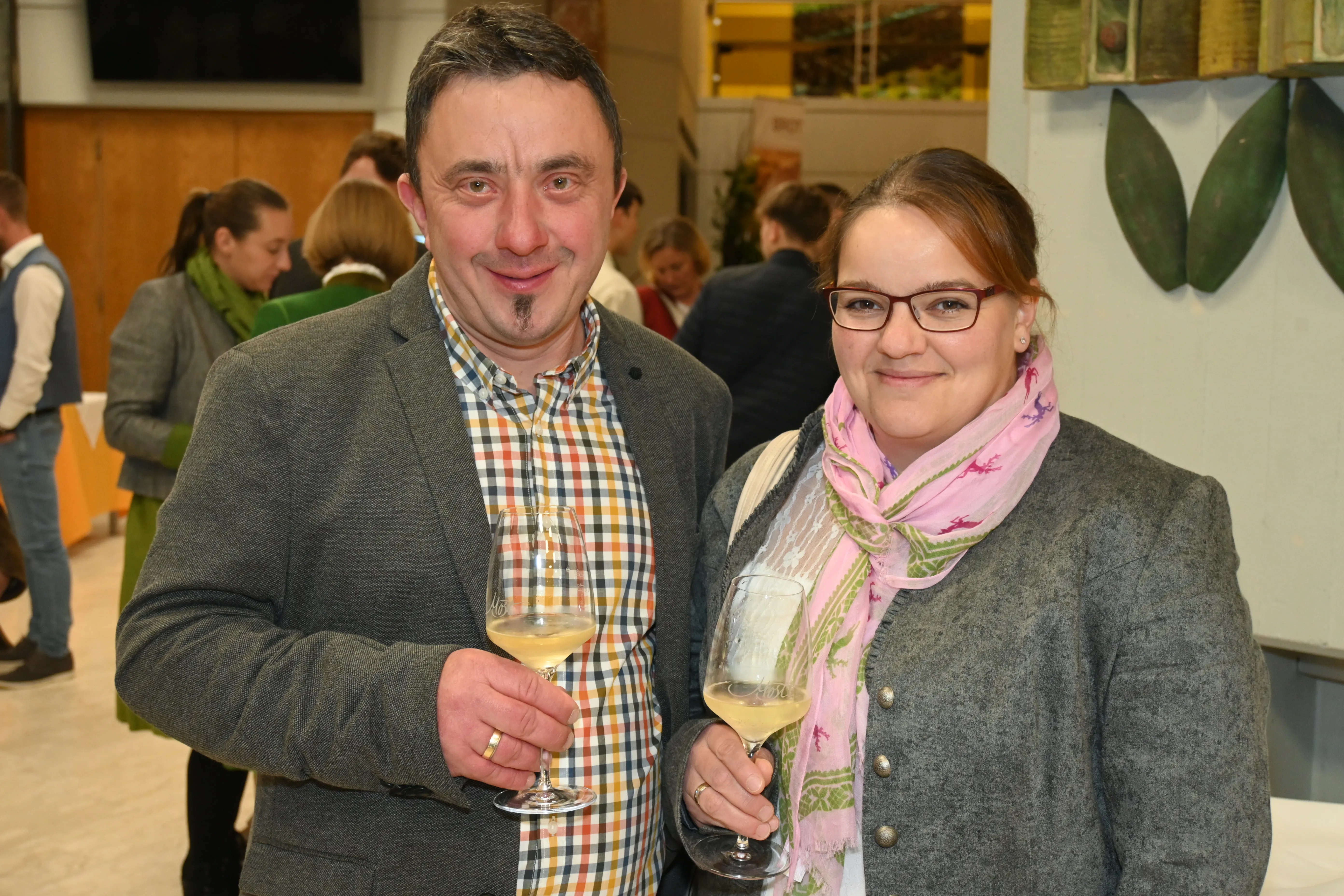 Herr und Frau Kettl stehen mit einem Glas Most und lächeln in die Kamera. Dahinter weitere Personen