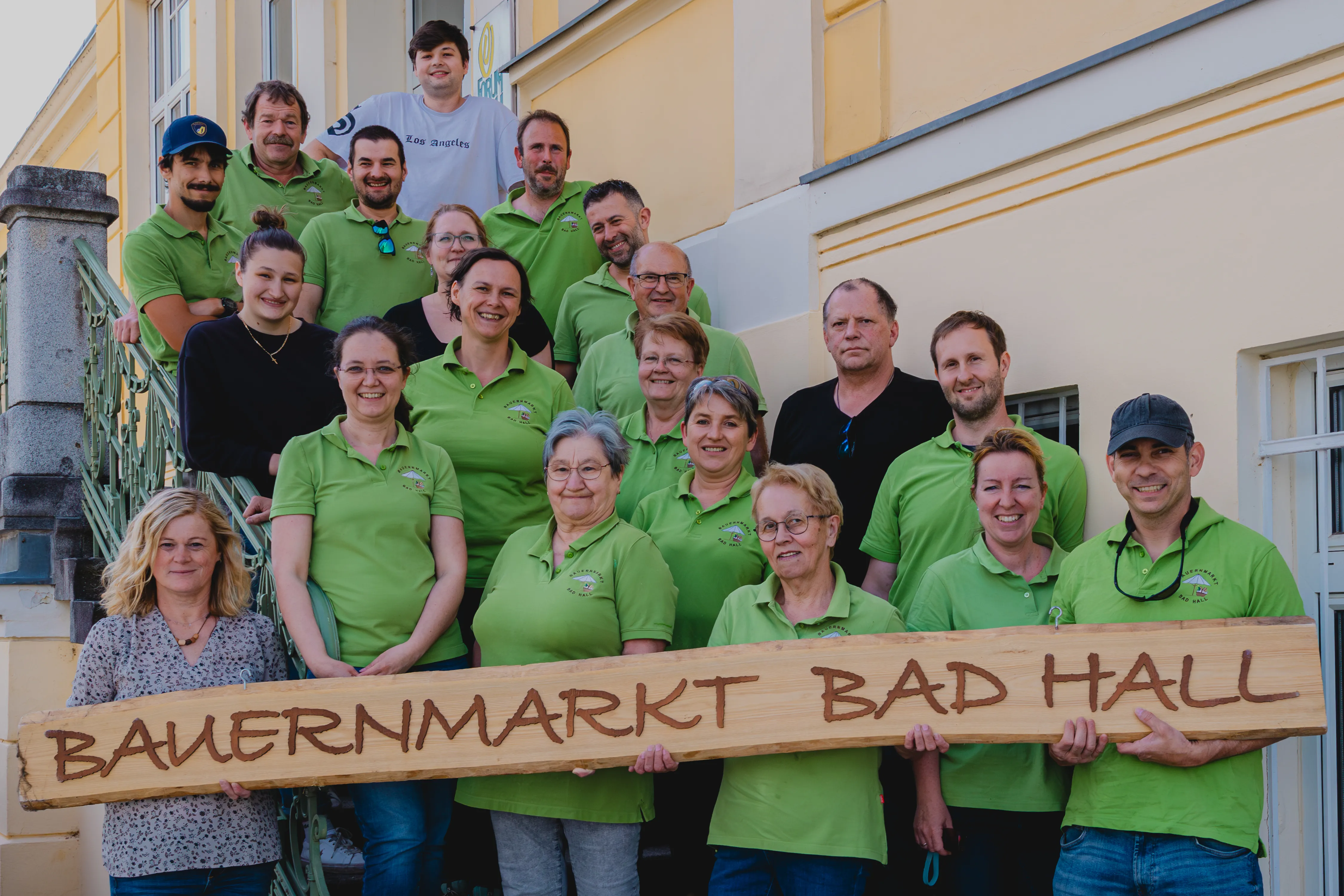 Auf einer Stiege stehen mehrere Personen im grünen T-Shirt und halten ein Schild mit der Aufschrift Bauernmarkt Bad Hall in die Kamera.