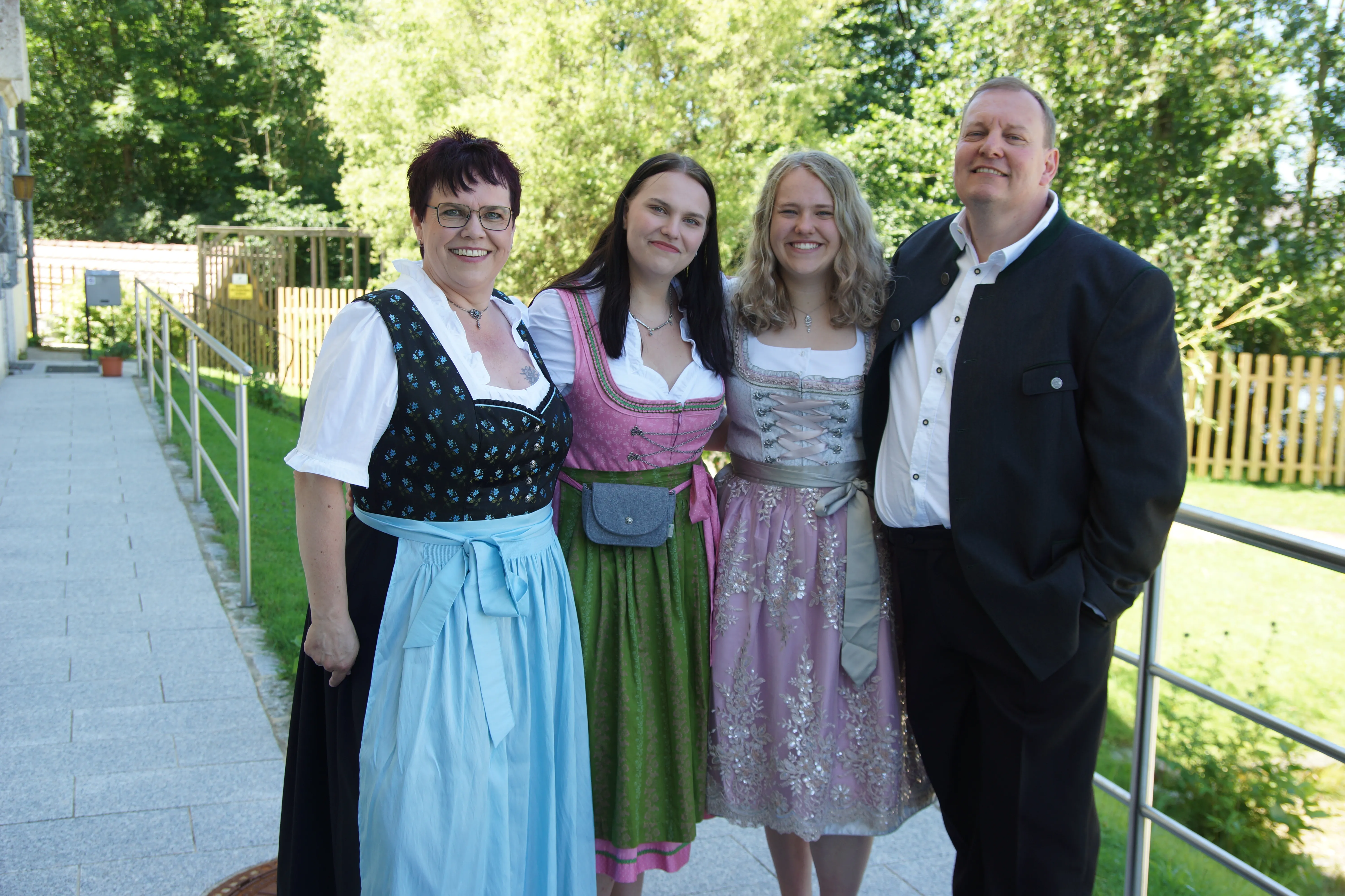 Ein Mann im Anzug und eine Frau im Dirndl stehen auf einer Terrasse; zwischen ihnen die beiden erwachsenen Töchter, ebenfalls in Dirndl