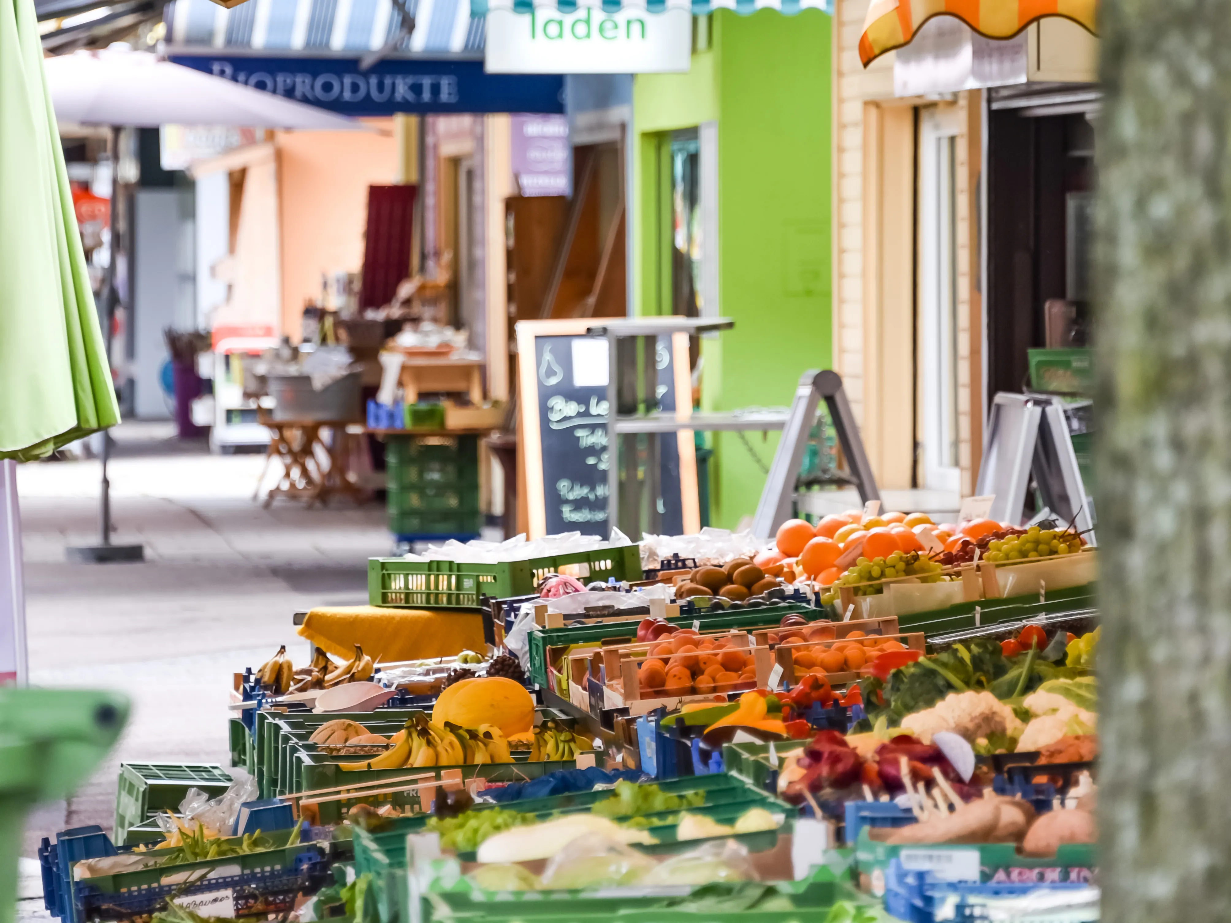 Man sieht viele verschieden farbige Marktstände mit Vordach; darunter verschiedene Waren