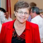 Christine Besenhofer mit kurzen braunen Haaren trägt eine rote Jacke, schwarze Bluse mit rotem Muster und eine Perlenkette.