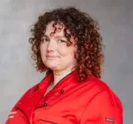 Romana Weber mit lockigem, schulterlangem Haar trägt rote Kochjacke mit schwarzen Knöpfen und schwarzem Besatz.
