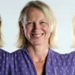 Bernadette Watzenböck mit schulterlangem, blondem Haar trägt ein lila Oberteil mit weißem Muster und eine dünne Halskette.